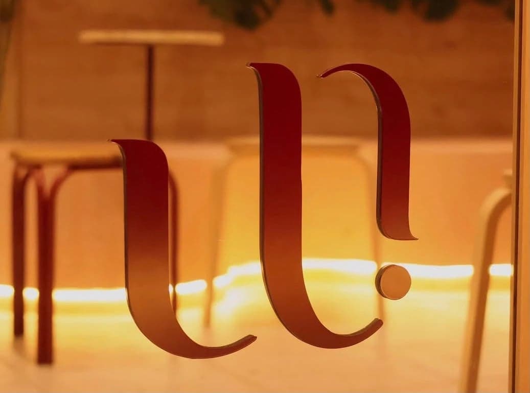 Logotipo de Uriarte en el vidrio con banquitos y luz cálida al fondo